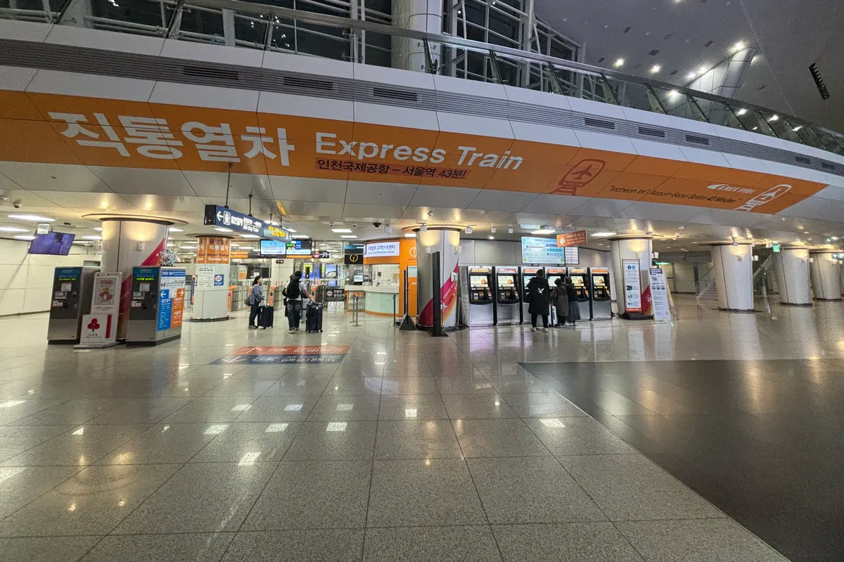 โถงขึ้นรถไฟด่วน AREX ที่สถานีอาคารผู้โดยสาร 1 สนามบินอินชอน มีตู้ขายตั๋วและนักท่องเที่ยวลากกระเป๋า