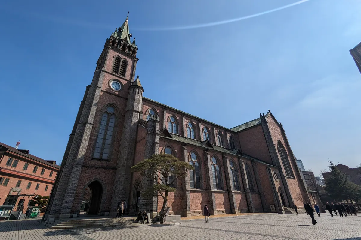 Red-brick Gothic Revival Myeongdong Cathedral and its bell tower under a clear blue sky