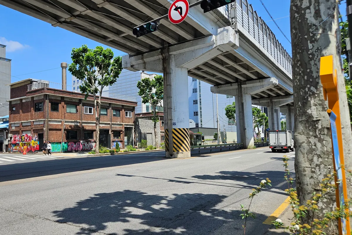 Elevated Seoul Subway Line 2 tracks over a Seongsu-dong road, next to an old red-brick building with graffiti