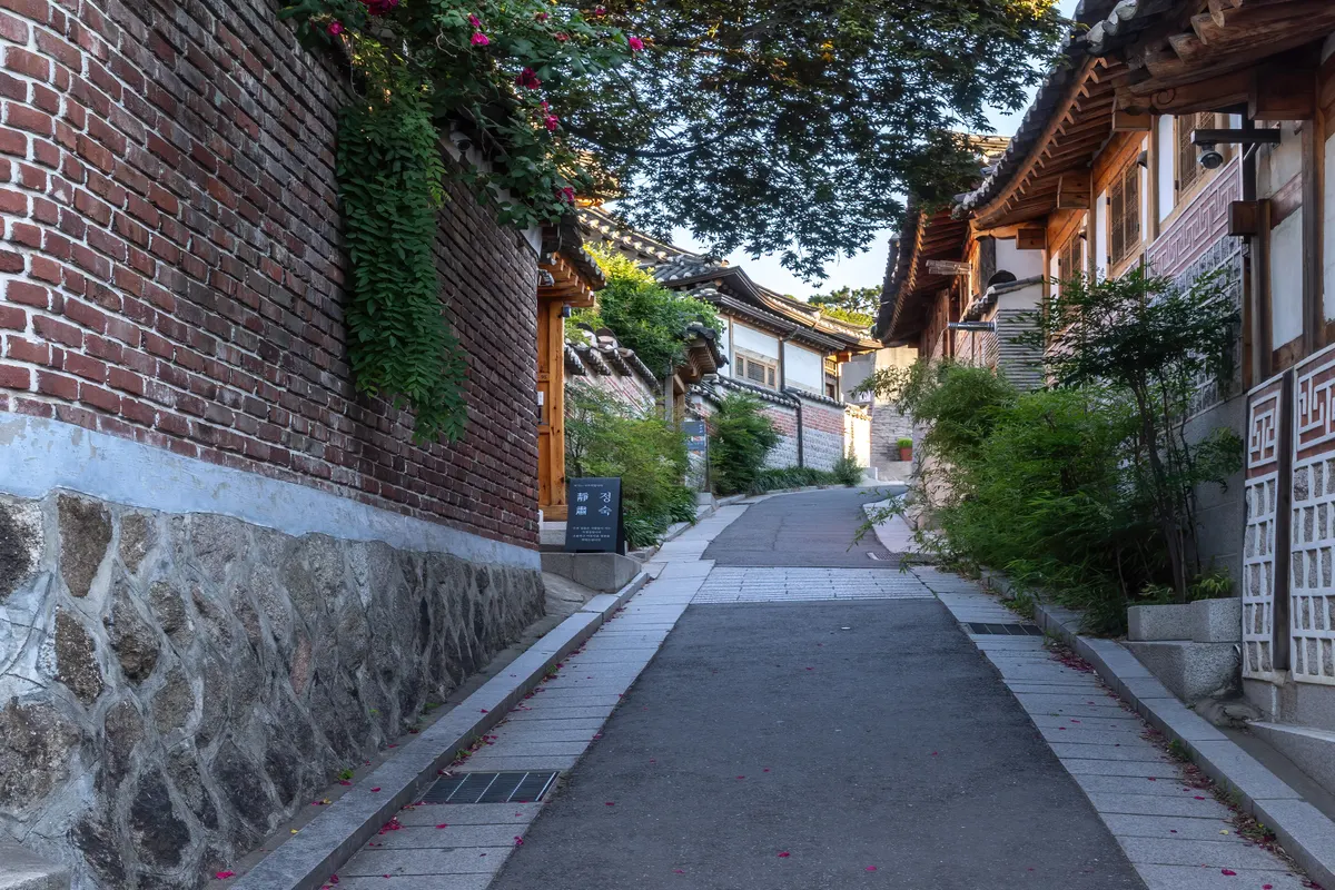 Quiet hanok-lined alley in Bukchon Hanok Village with roses spilling over a brick wall